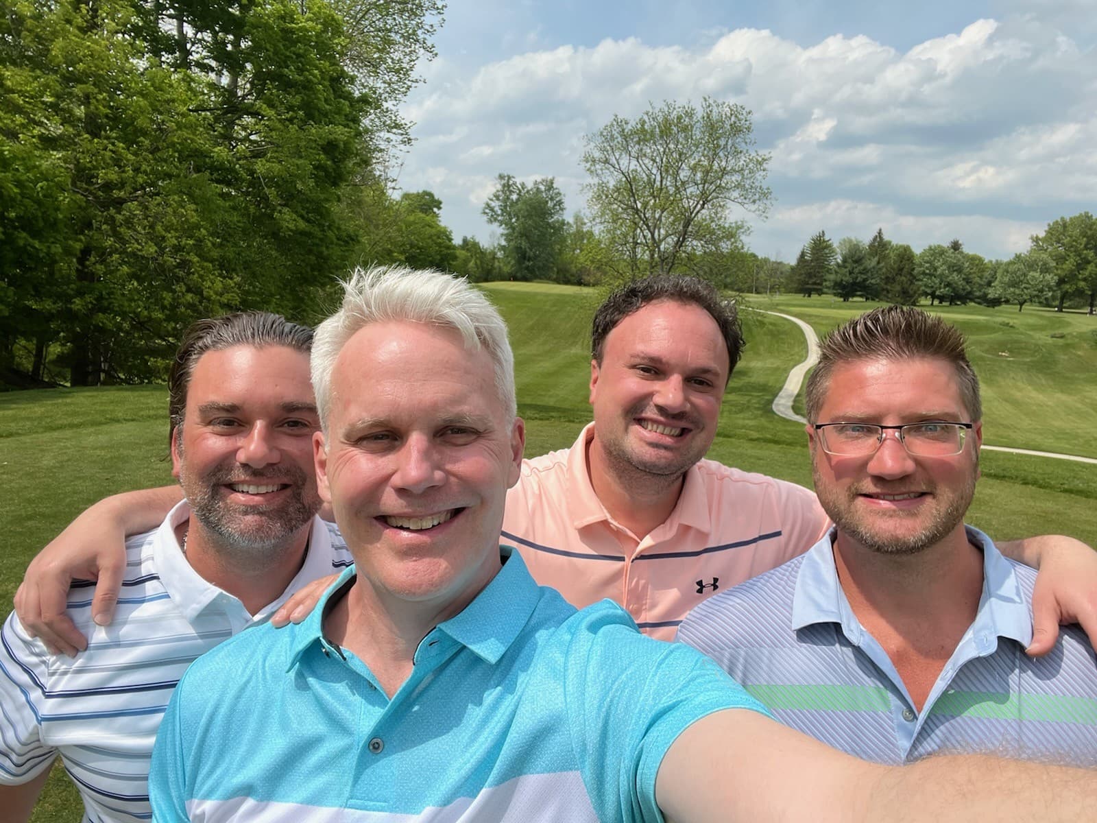 Four golfers smiling together on a par 3 tee box