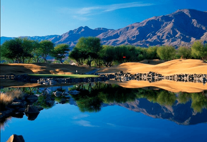 Traditional golf course with lake reflection and mountains in the background